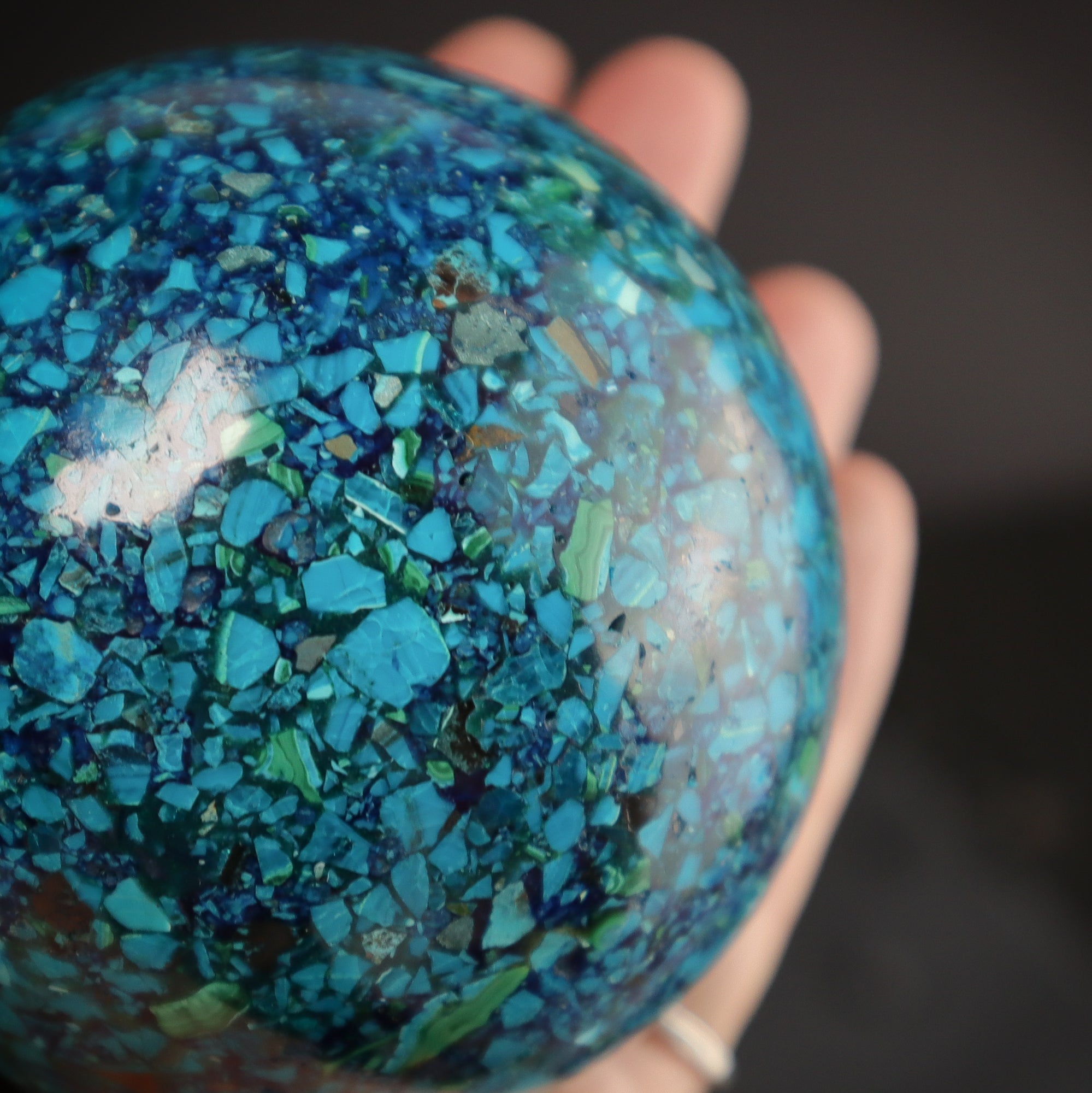 Close-up of a Chrysocolla sphere in a hand.