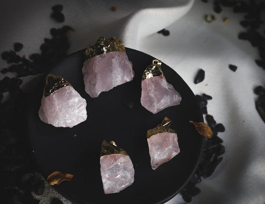 Raw rose quartz pendants on a black pedestal