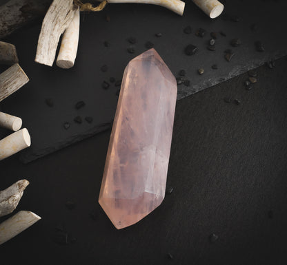 Rose quartz wand on a dark table and dry wood.