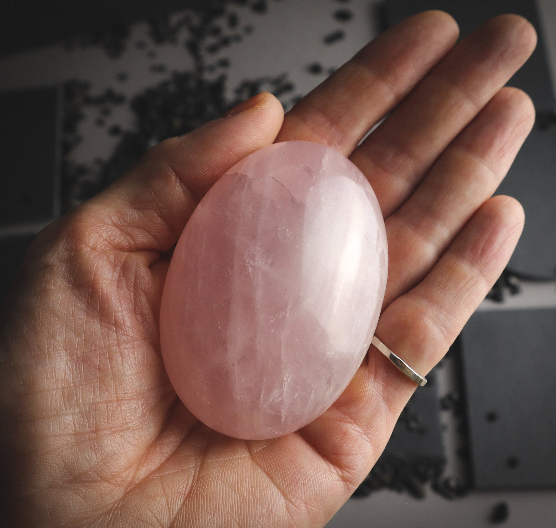 Pink mineral palmstone on a hand with an artisanal ring.