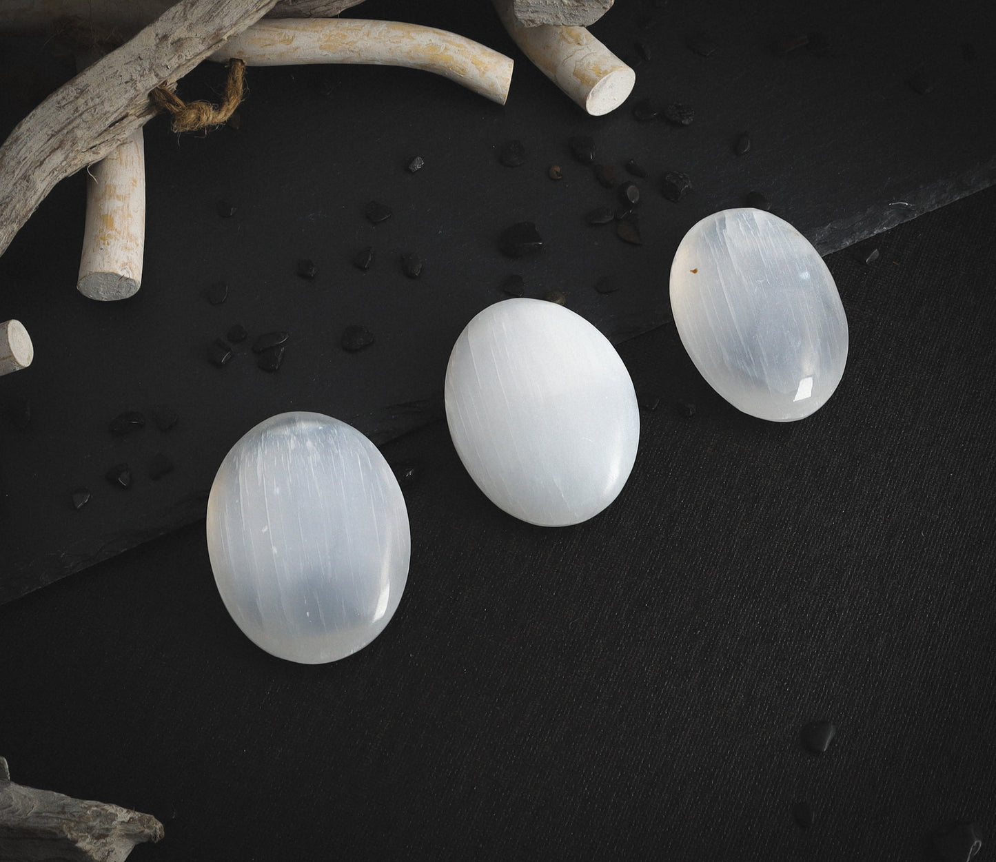 Selenite palm stones on a dark table.