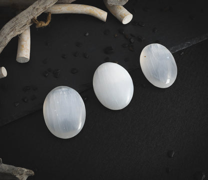 Selenite palm stones on a dark table.